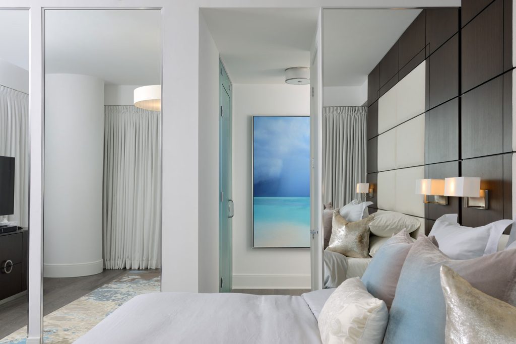 View across a bed made with gray linens to the hallway outside.
