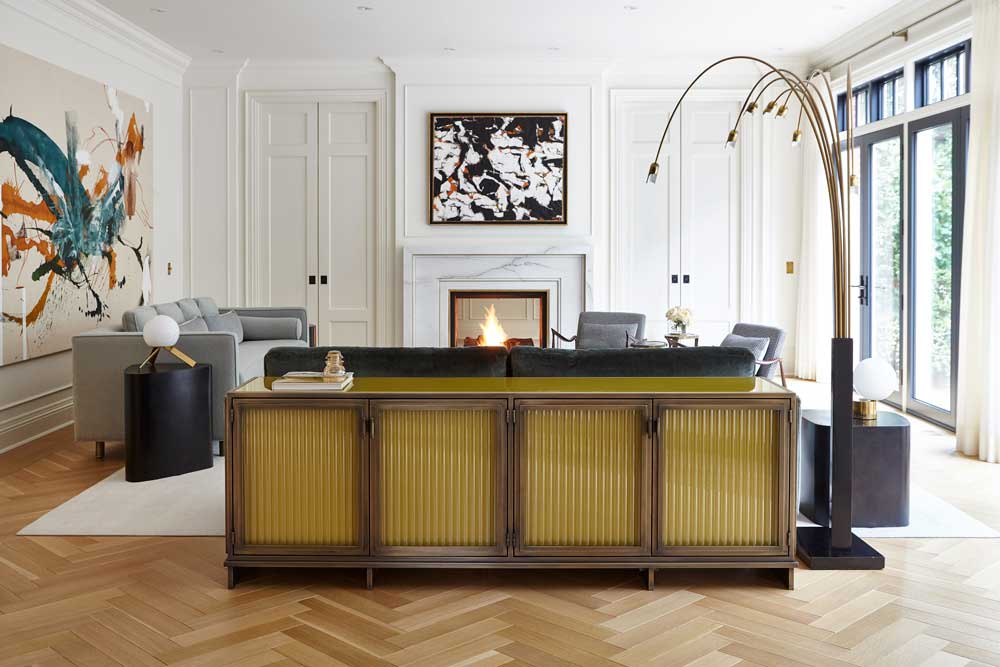 Living room with hardwood laid in a herringbone pattern, white walls with crown moulding, and gray sofas. A brass lamp with a black pedestel over hangs the three seater sofa.
