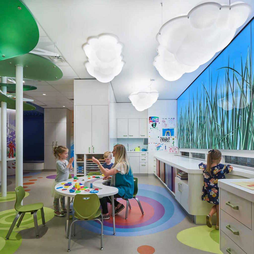 Open play area at SickKids PlayPark with cloud shaped lights, and kids playing around a table with blocks.