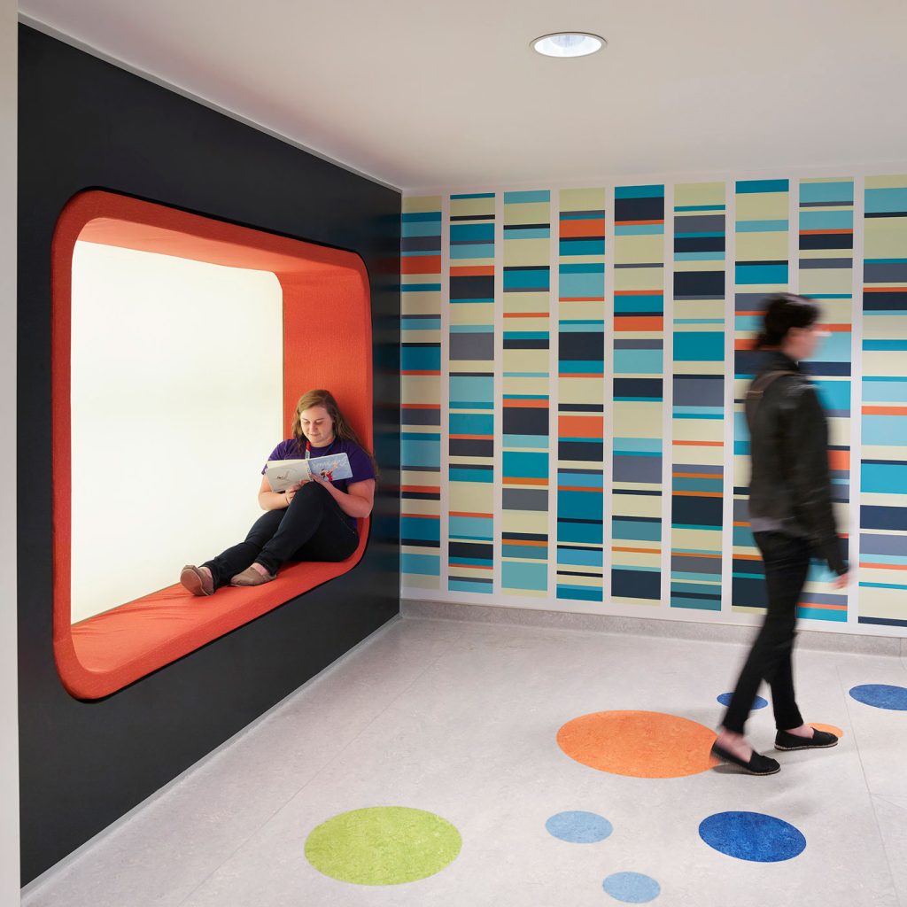 A padded orange alcove provides a seating nook next to a blue, orange and yellow linear graphic on the wall.
