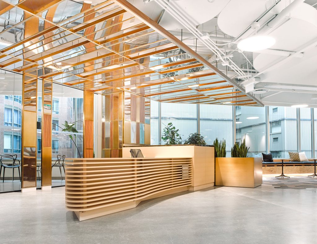 Reception desk made of horizontal wooden slats and mirror panels behind and above the desk drawing light and attention to the desk