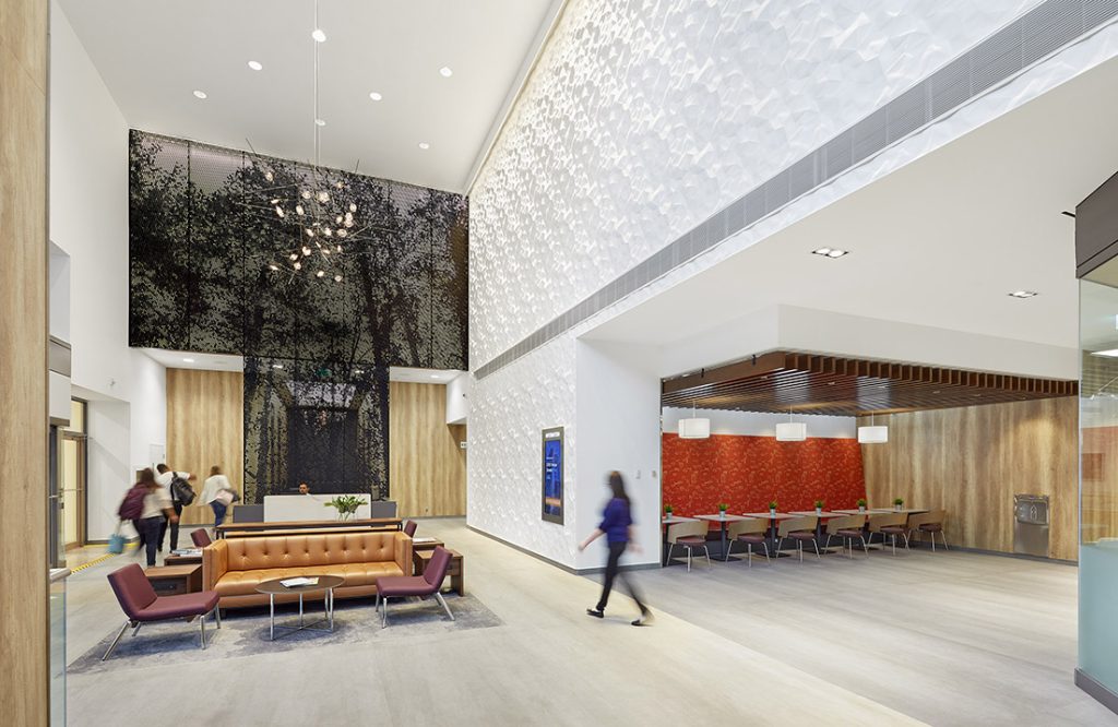 View of the entire lobby from the main entrance, where the black finish metal screen, the white 3D textured white wall, the lounge/waiting area and the small cafe are all visible and beautifully contrast each other.
