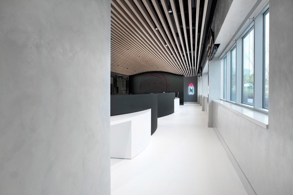 Custom ceiling framework in a form of slats leading the eye to the black feature wall branded with a discreet 3D raptors logo outline on the other end of the space.