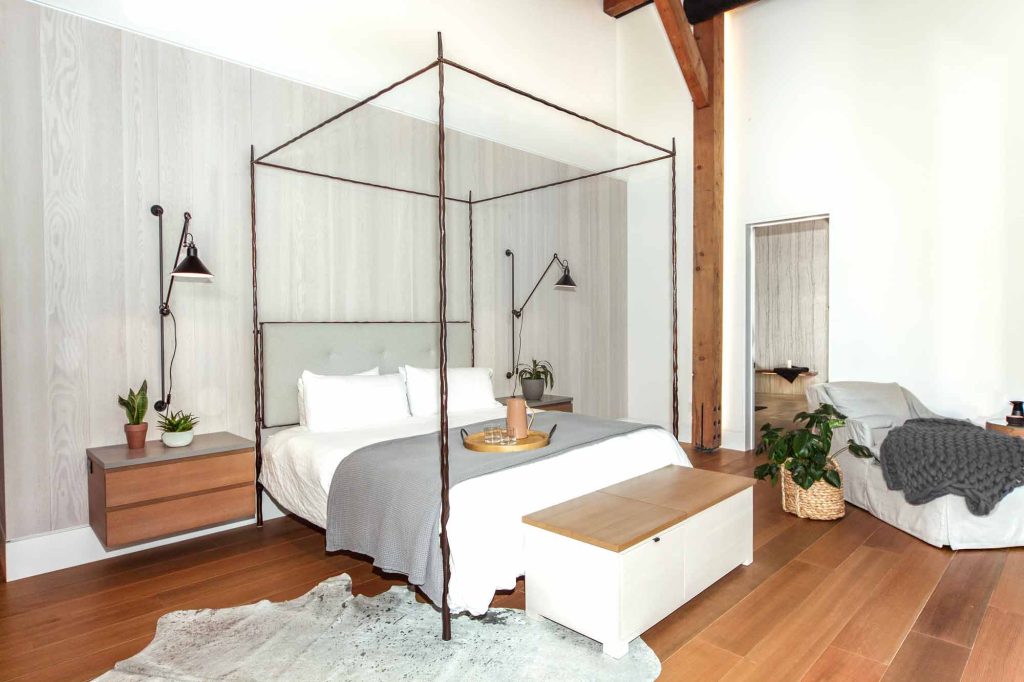 Large serene neutral bedroom with accents of wood, and a contemporary four post bed in the centre, with natural materials throughout