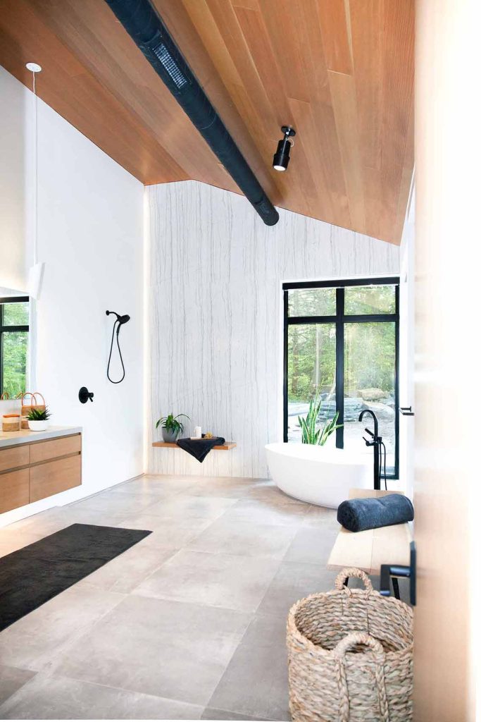 Large bathroom with natural finishes throughout, wood ceilings, granite floors and stunning feature wall. Standalone tub is by a large floor to ceiling window.