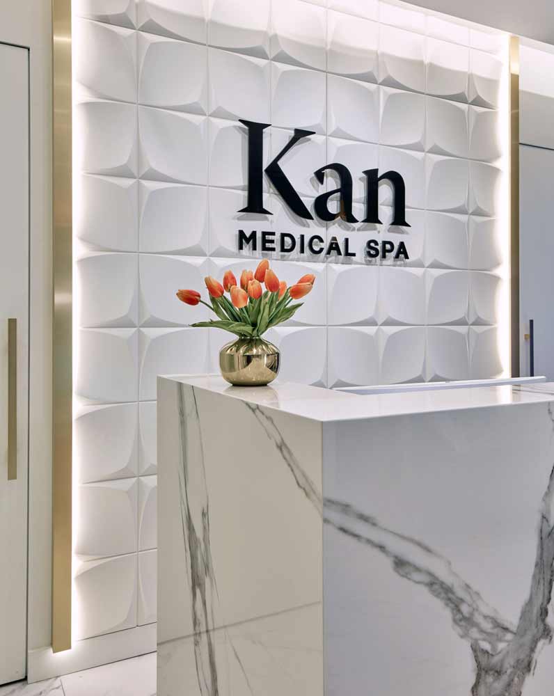 Closer side view of the reception desk and a golden vase full of orange tulips on top. The geometric feature wall and logo are visible behind the desk.