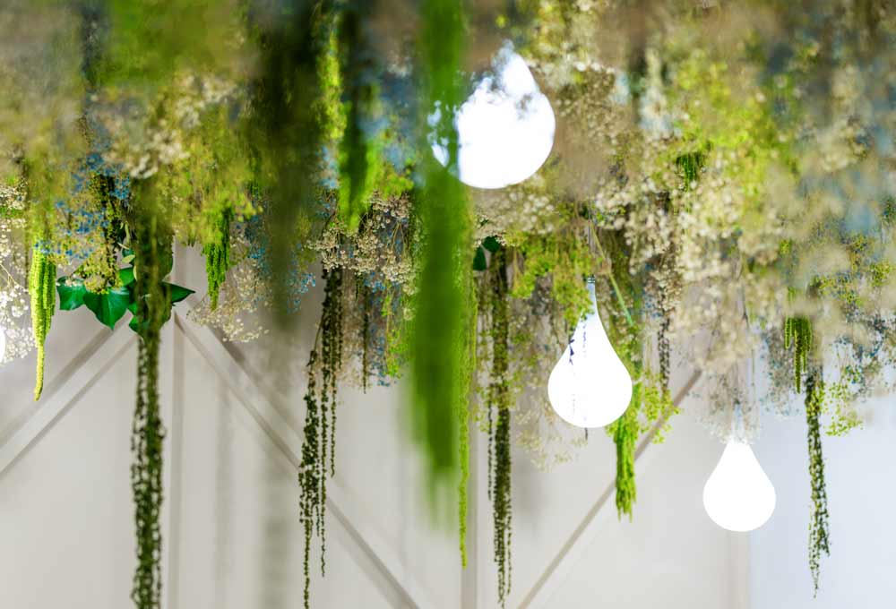 Close up of the biophilic design hanging down from the ceiling with choreographed undulating light-droplets peeking through the greenery