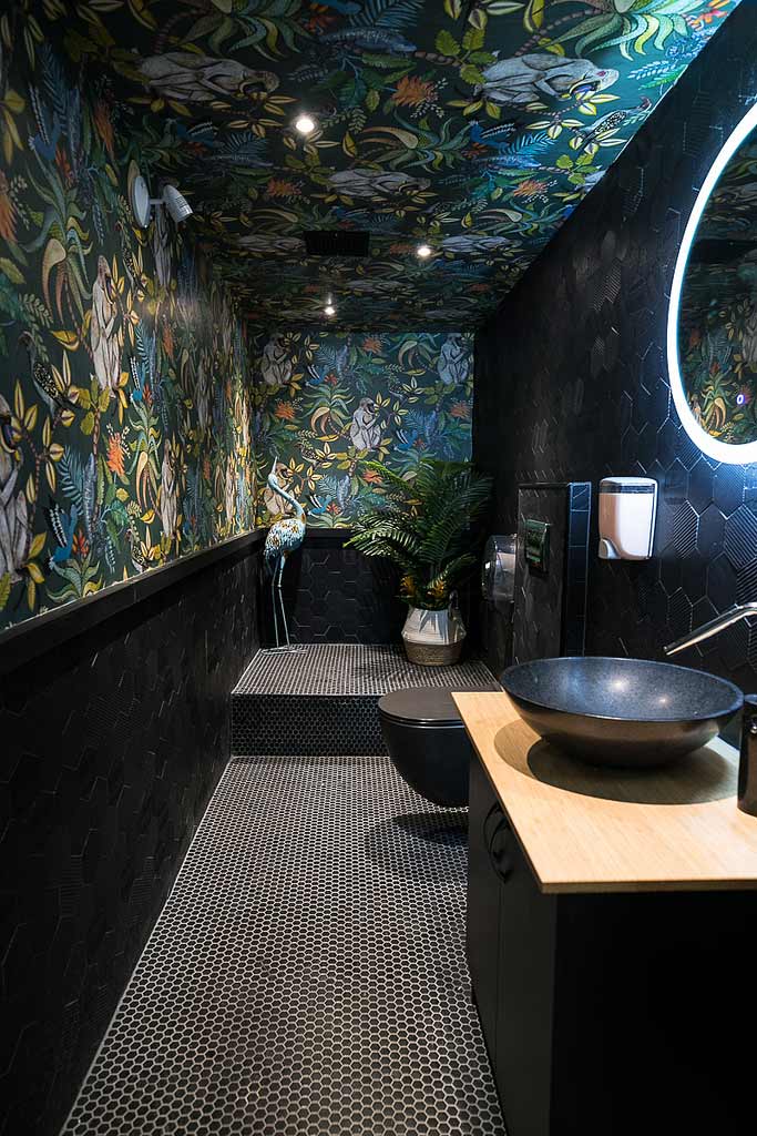 dark monochromatic material finishes with a jungle themed wallpaper in the washrooms
