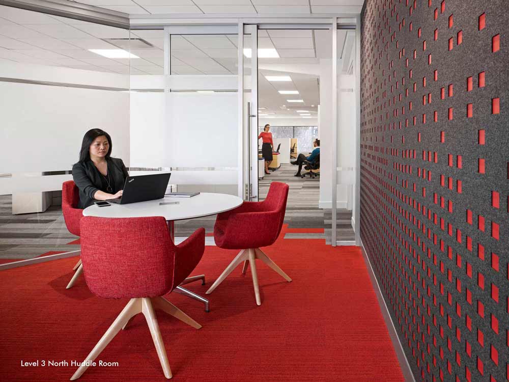 A huddle room in predominantly red color scheme, encased in a glass wall with privacy film