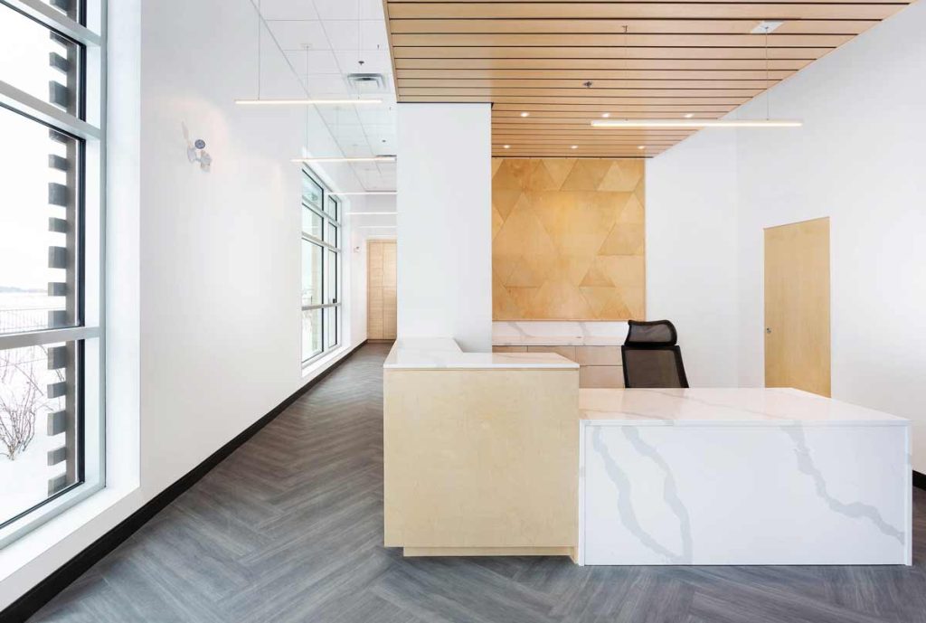 View of the reception desk from the waiting area. Desk is done in marble and wood combination of materials and a wooden slats detail above, and a textured wood detail on the wall behind.