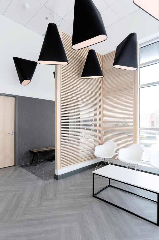 Waiting area featuring an L shaped wood detail to create a screen like effect between the front window and reception/waiting area. Above are hanging several black triangular light pendants