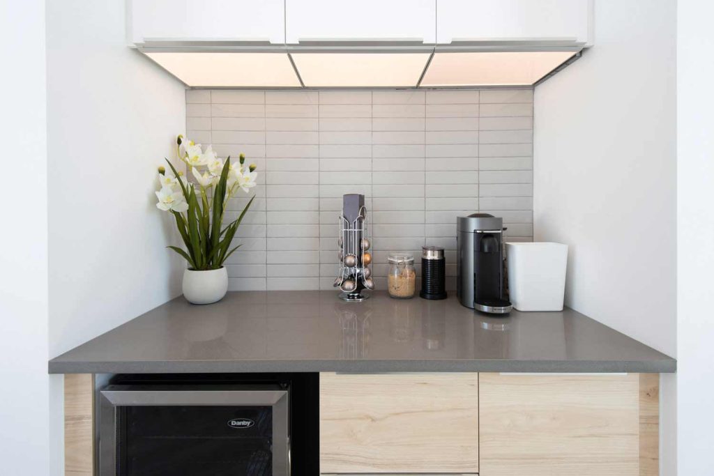 A little wet bar to serve coffee and drink to clients. Bottom cabinets are in light wood finish and top cabinets is white, with a warm gray countertop