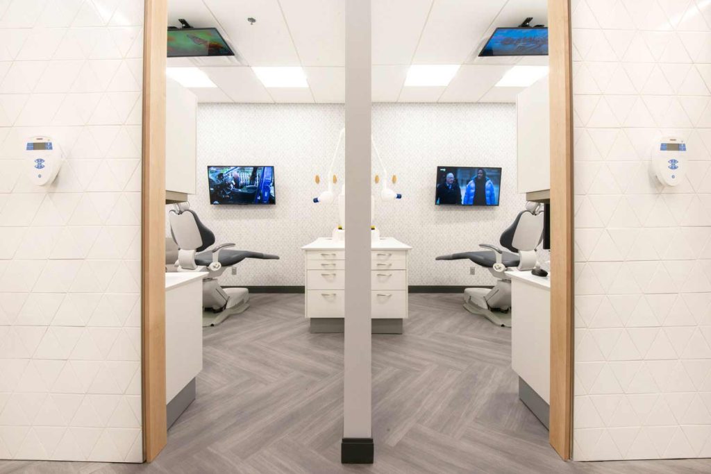 Two adjacent predominantly white treatment rooms with wood finish flooring that adds warmth to the space