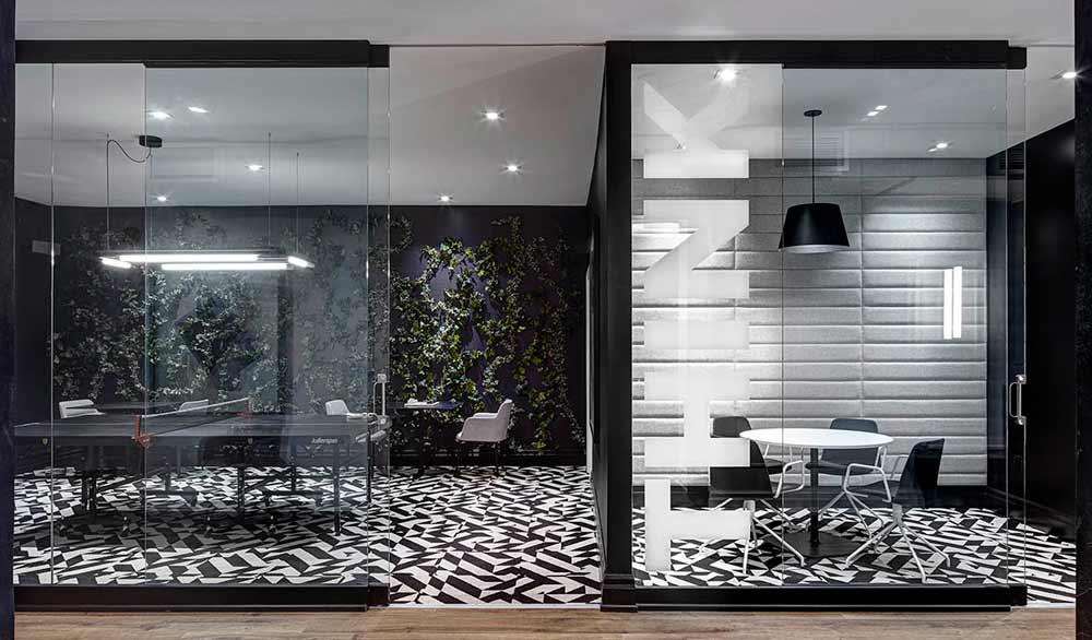 Two adjacent playful spaces enclosed by glass walls, in a predominantly black and white color scheme with some biophilia on the wall