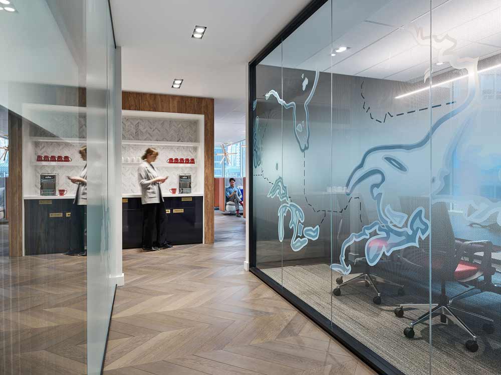 A hallway leading to a communal lounge with offices on both sides featuring illustrated maps of Canada on their glass walls