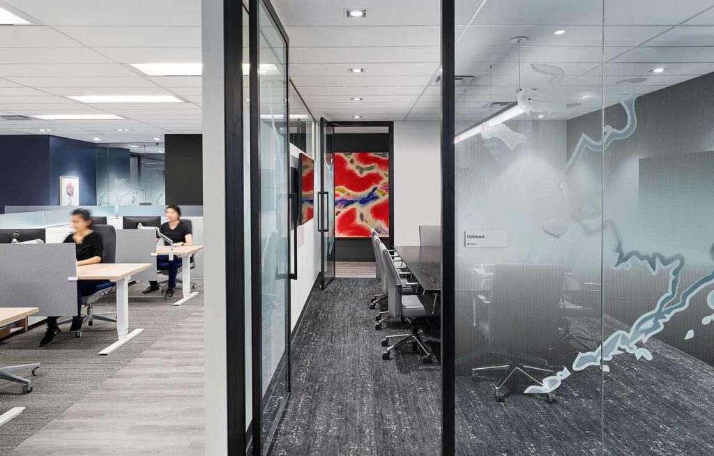 A modern work station area and next to it a meeting room entrance featuring illustrated map of Canada on the glass walls surrounding the meeting room