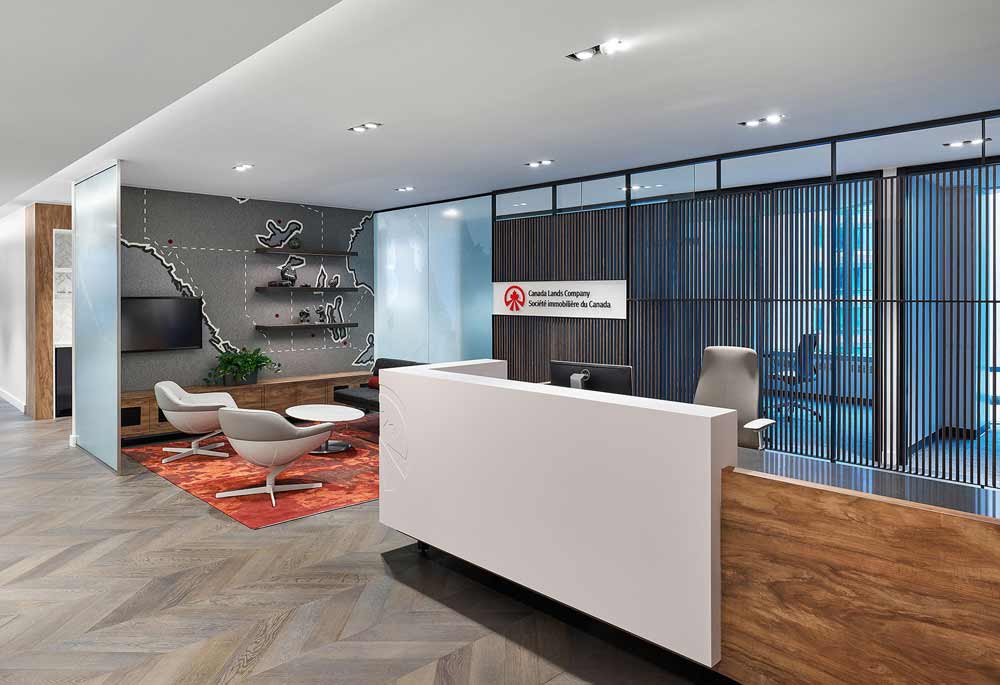 Contemporary reception area with warm accents wood finishes, red tones, a modern reception desk and waiting area with a large felt map of Canada across the entire wall