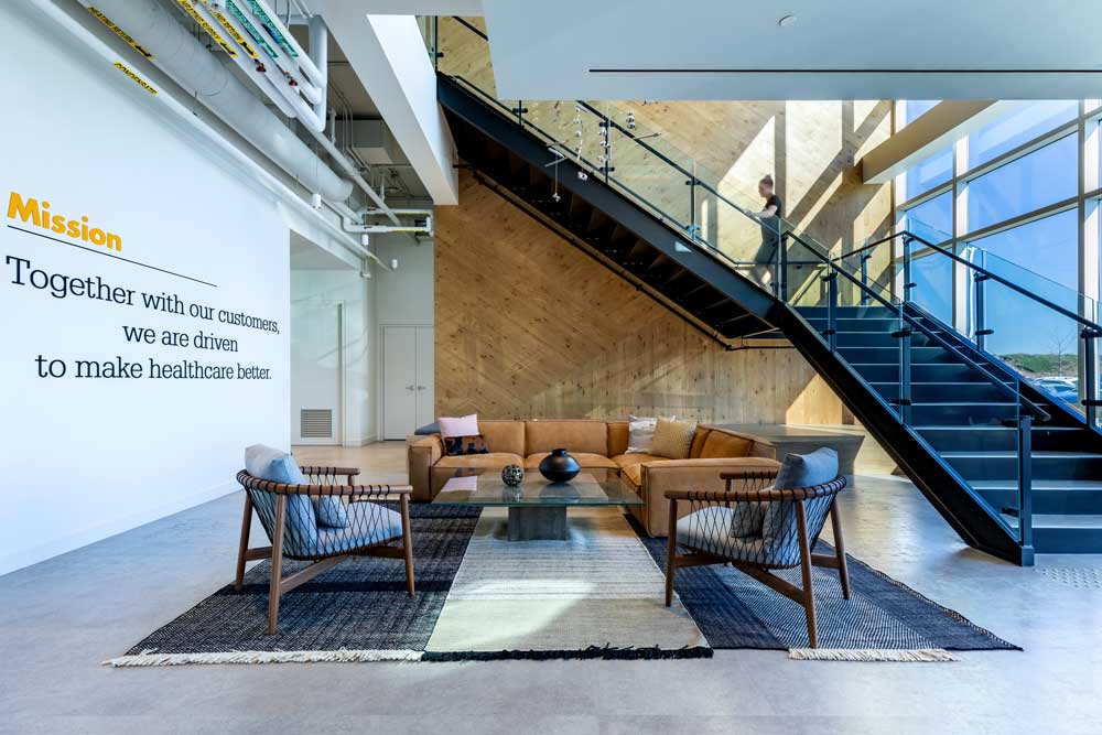 Lounge are in the main lobby area at the bottom of industrial looking black staircase with glass railing against a wood finish wall