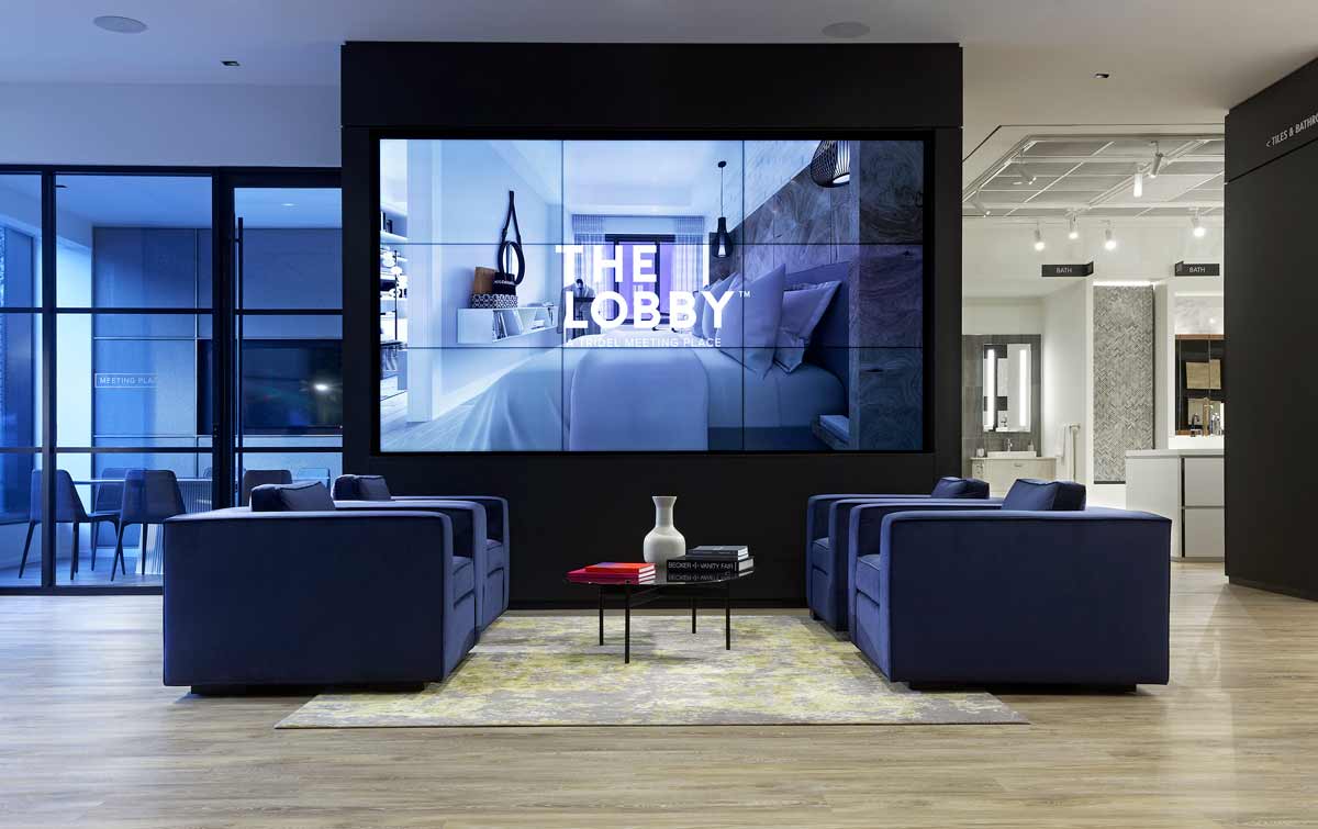 Lounge and waiting area with large comfy blue lounge chairs and a large multi-digital screen unites the entrance with the showroom environment