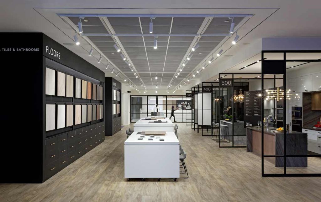 Comfortable and flexible showroom environment with the space divided into sections with glass screens on one side, large tables with seating down the center and walls with samples along the other side.