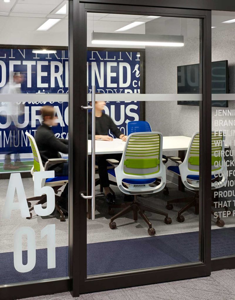 Small collaboration office behind glass walls and door, with office furniture in corporate Go Easy colours