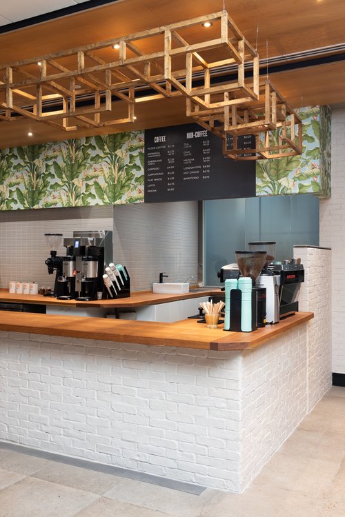 View of the white brick counter from the main entrance, wooden squares hanging above the counter and the menu with organic leafy wallpaper