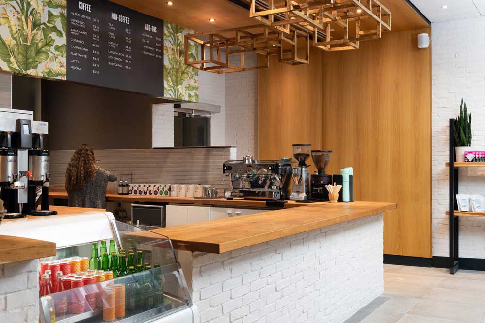 White brick counter looking towards the espresso machine and wooden wall detail behind that runs all the way to the ceiling above the counter area