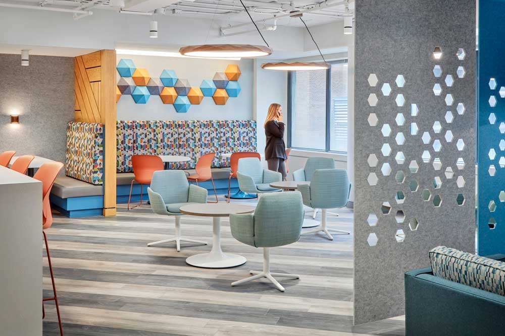 View of the entire cafeteria area in a blue, orange and gray colour scheme and separated from the lounge area by gray panels with hexagon details