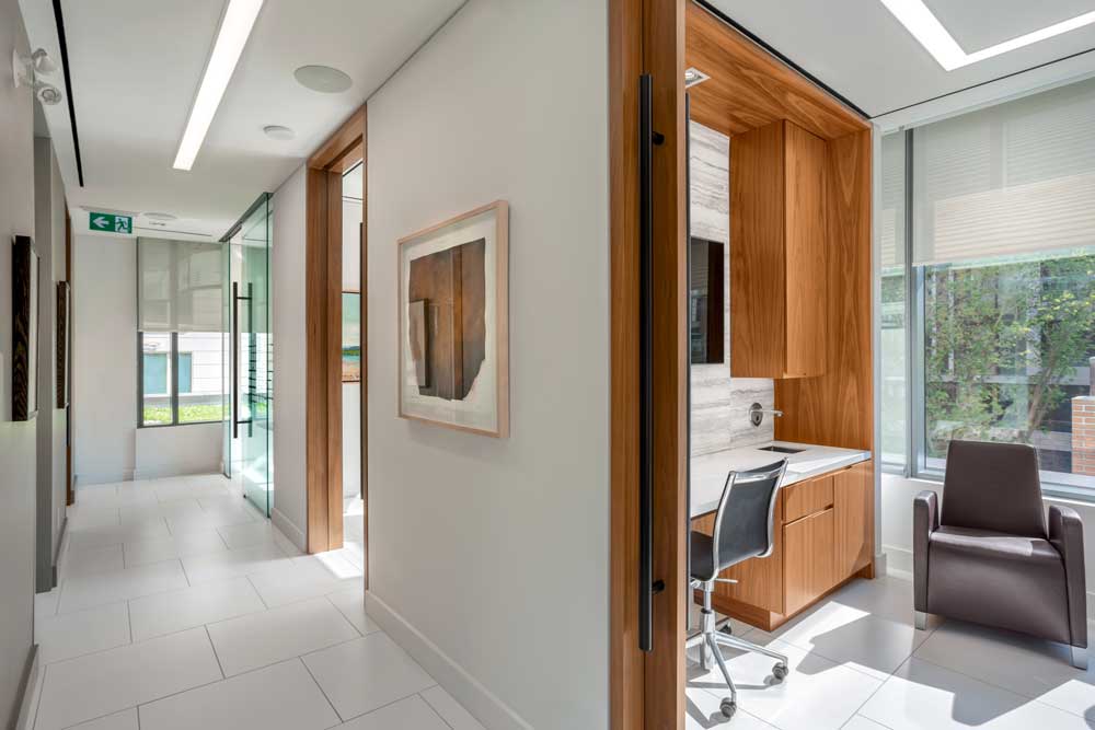 View of one of the offices and walnut veneer custom cabinetry with black hardware looking in from the white walled hallway