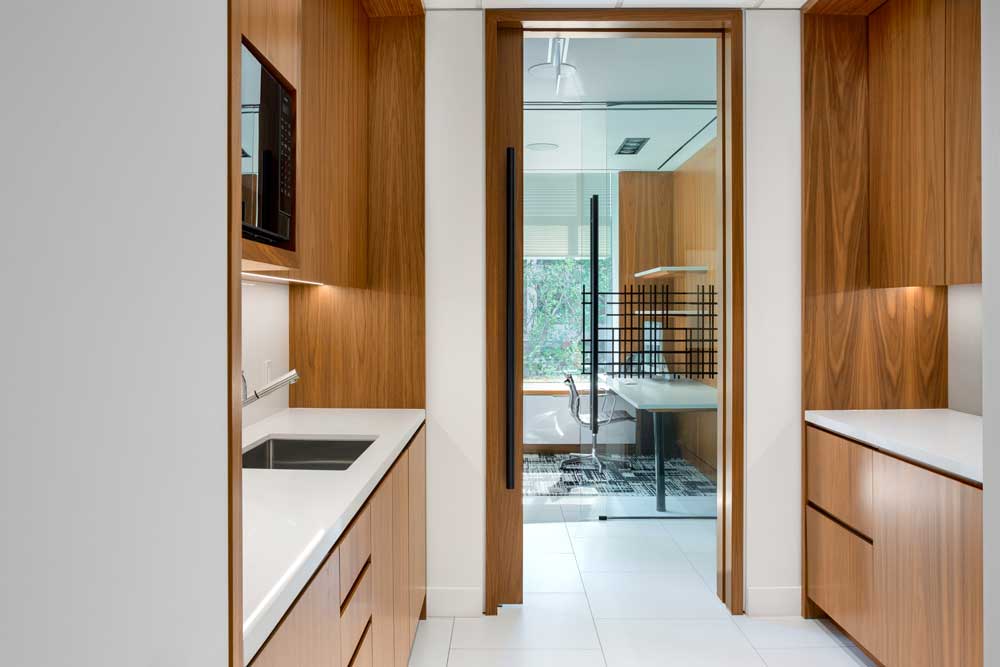 Walnut veneer cabinetry in the kitchenette with black hardware consistent with rest of the office space