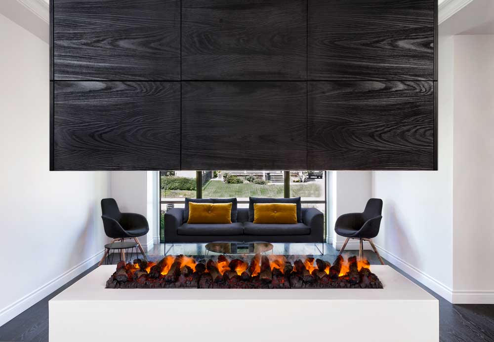 A view of the main living room area through the vapor fireplace is set in a crisp white pedestal and topped with a sleek black hood that doubles as storage