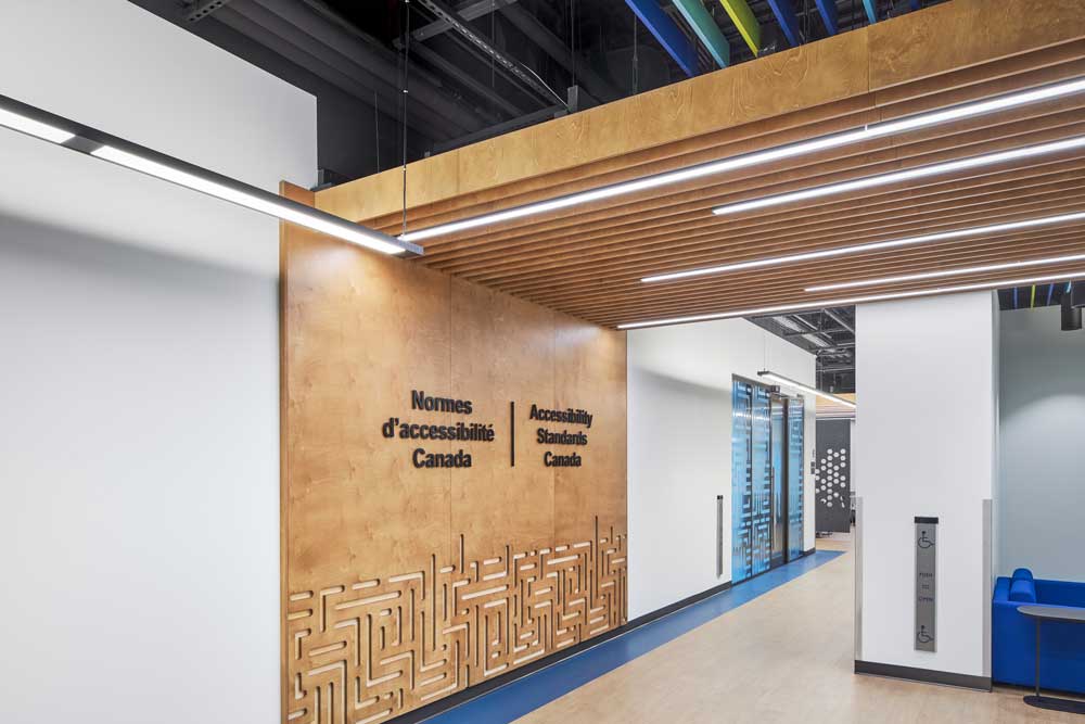 Accessibility Standards Canada reception area with wood coloured slatted ceiling detail that connects to the branded wall feature