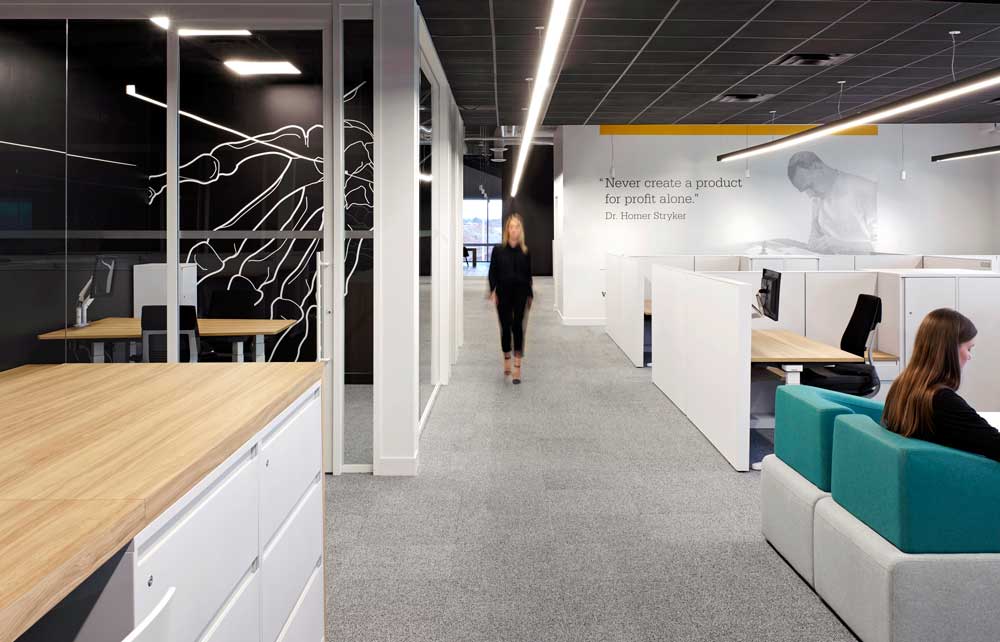 Work station and collaboration area in a predominantly neutral color scheme with pops of yellow and green as accents in wall graphics and furniture pieces
