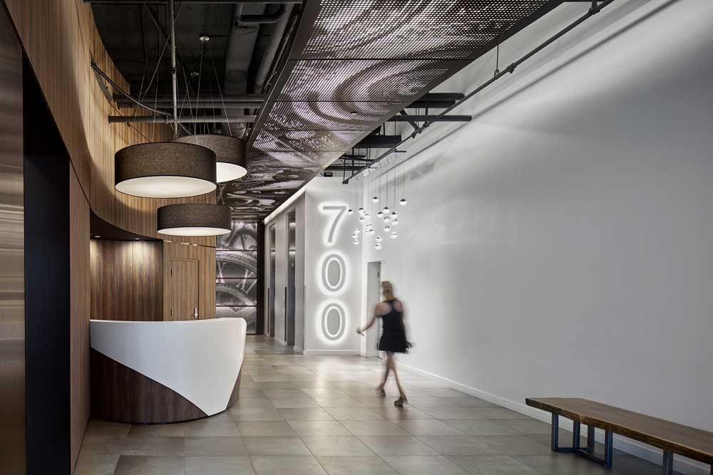 Tall wood paneling on the walls behind the security desk leading the eye up to the clock detail graphic on the ceiling and to the large building number sign on the wall leading to the elevators