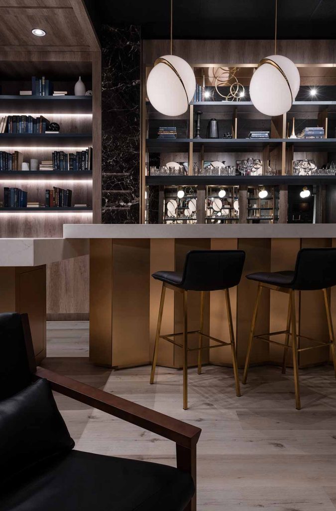 A vignette of the white island counter top and golden base with elegant gold and black bar stools. Above are hanging round pendant lights