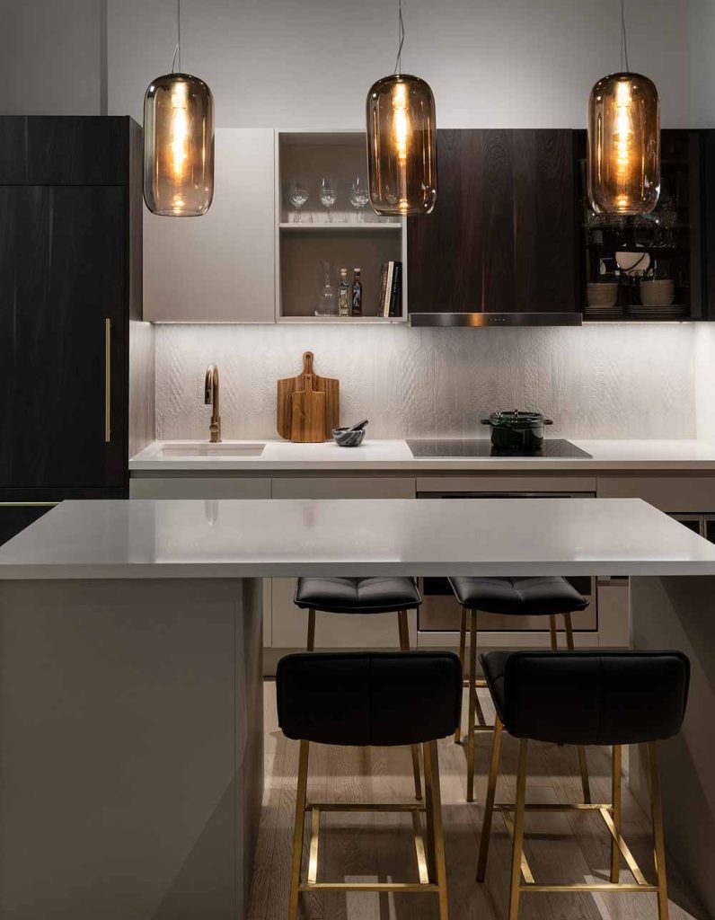 A detail of the model kitchen design in dark and light contrasting color scheme and statement light pendants above the island