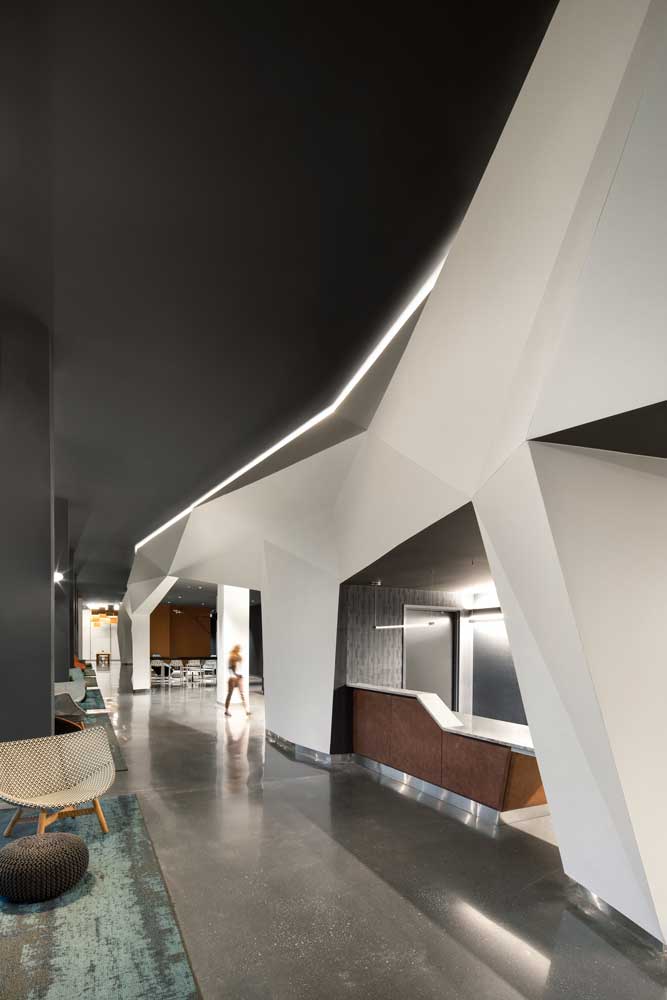 Main lobby featuring a white backlit geometric ceiling detail against the black ceiling above the security desk that is tucked under it