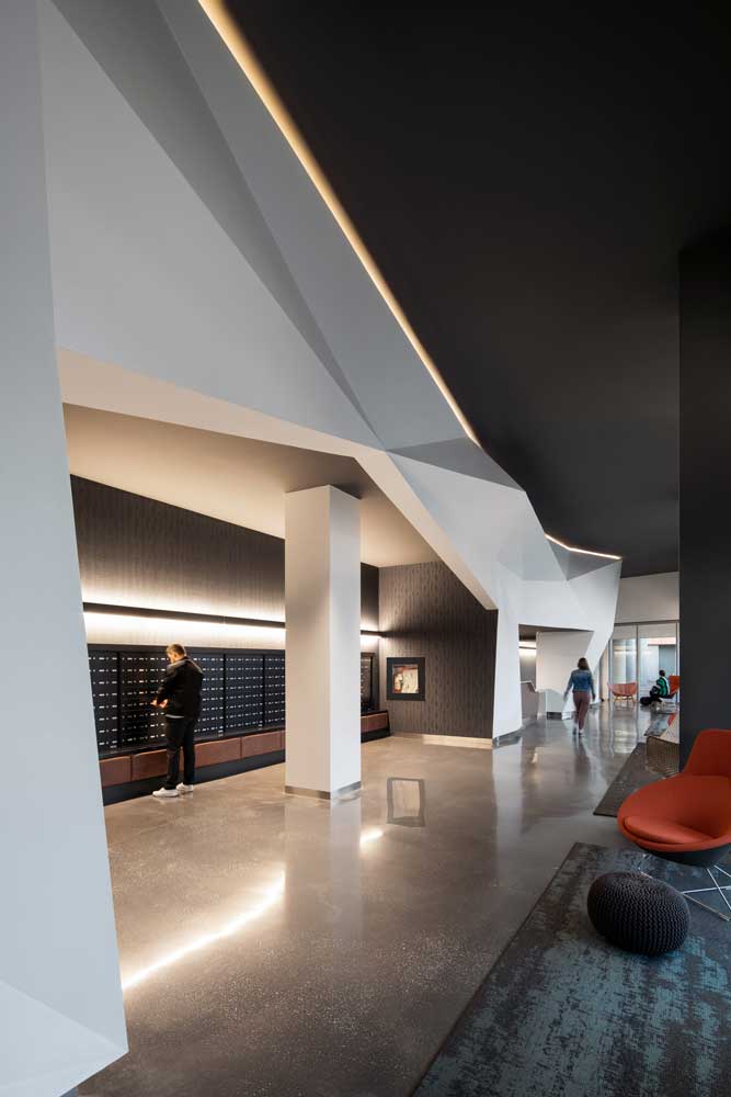 Main lobby featuring a white backlit geometric ceiling detail against the black ceiling, and furniture in accent colours of red and teal