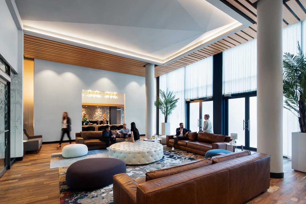 A view of the party room's large central seating area with leather sofas an ottomans, beautiful floor to ceiling windows making this space airy and bright