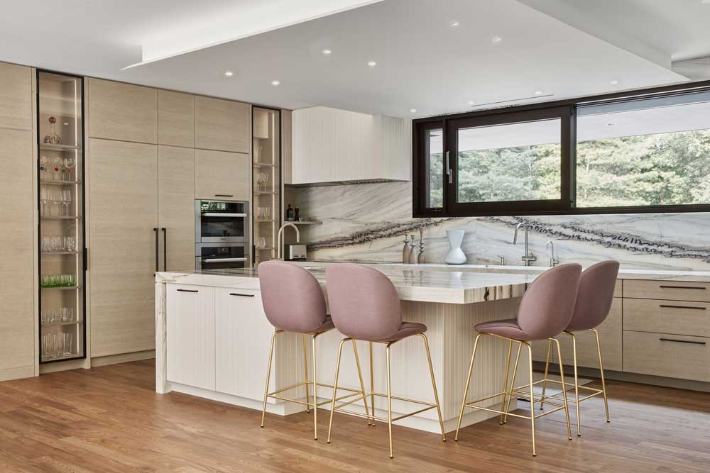 Panelled walls, built-in appliances and secret doors to pantries and storage were artfully designed in the
bright light filled kitchen. Powder pink bar tools at the island add a pop of colour in he space and the backsplash adds movement with its veining.