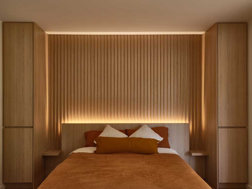 Bedroom details of the bed and the wooden slat wall detail above the bed. On both sides are floor to ceiling cabinets made of the same wood panel material