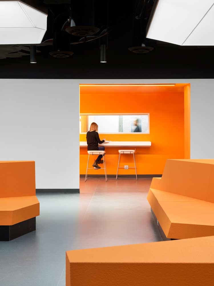 Narrow hallway room adjacent to the lecture hall lined with bar height table along the wall, as seen from the main lecture hall