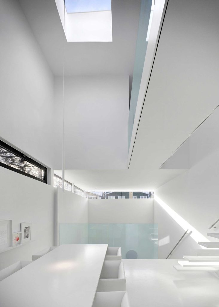 A view from the kitchen direction toward the dining table on the main level and the triple height living area walls. A skylight is visible above