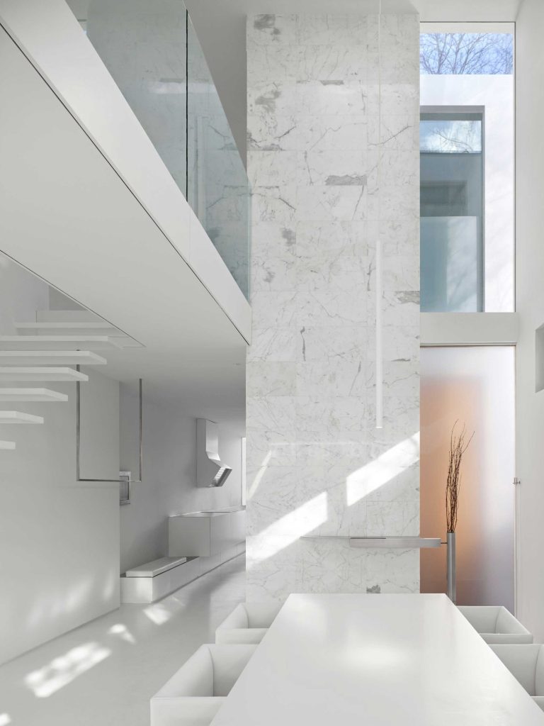 Dining area with the kitchen visible in the background, and the glass railing above on the bridge leading to bedrooms on the upper level. There are narrow windows all around letting the light in