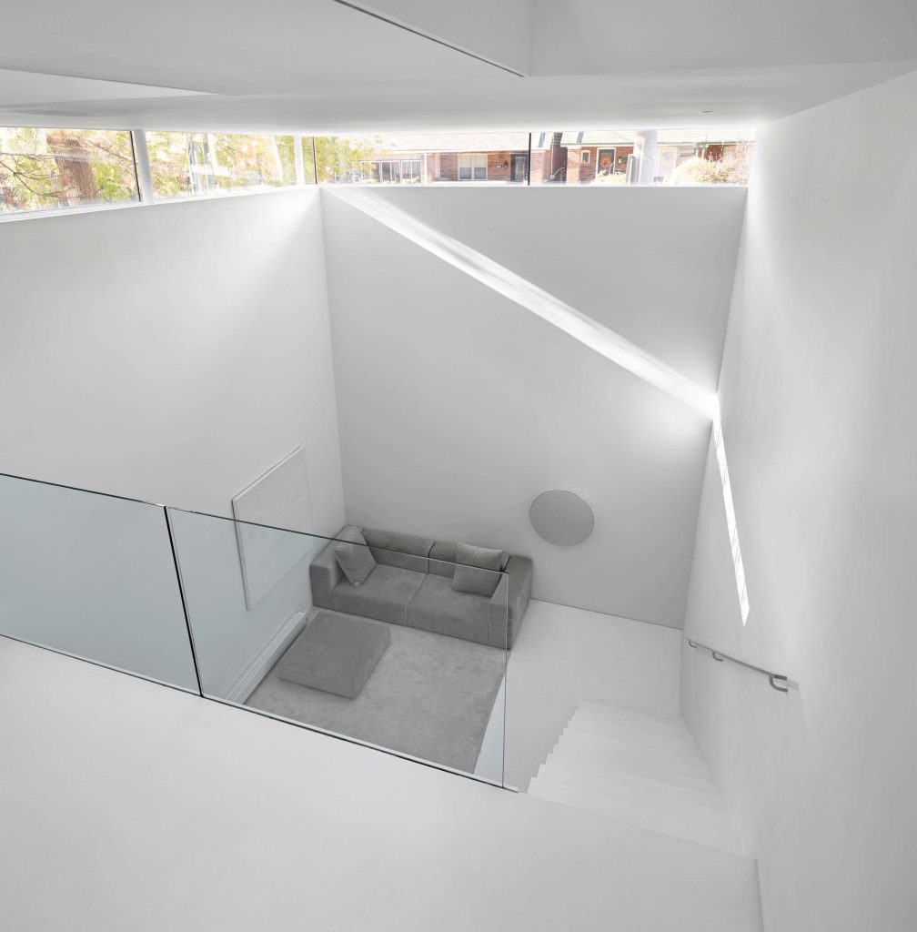 A view from the stairs looking down at the living area and the tall ceilings with the thin strip of windows letting the light in