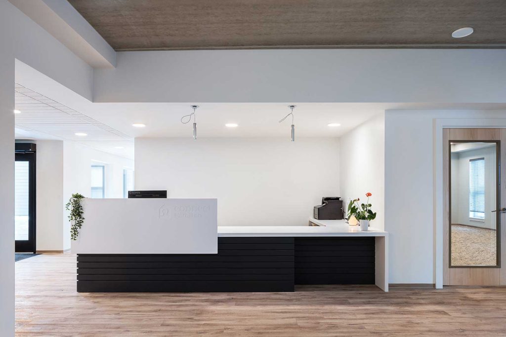 Reception desk in a black and white colour combination with modern sleek lines against the warm wood on the floors. Warm coloured wood finish is on the ceiling above