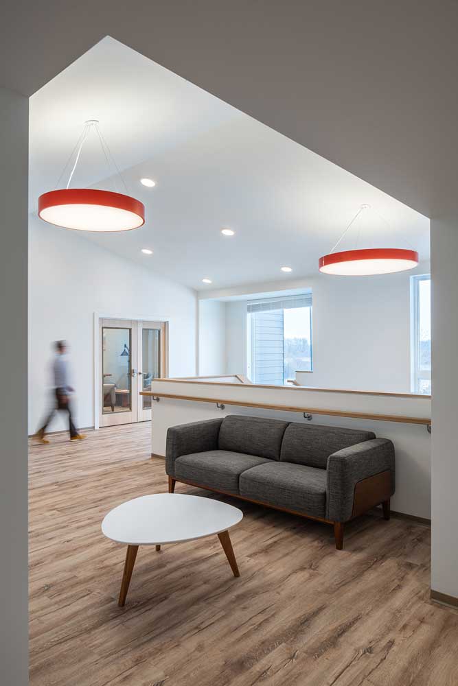 A hallway area with comfortable seating, modern circle shaped pendants in red above, warm coloured wood flooring, and a ton of natural light