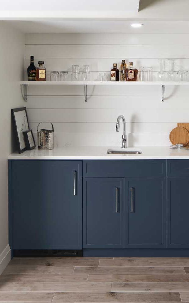 Wet bar in the basement with dark blue/gray bottom cabinets and white shiplap backsplash behind open shelving for drinks