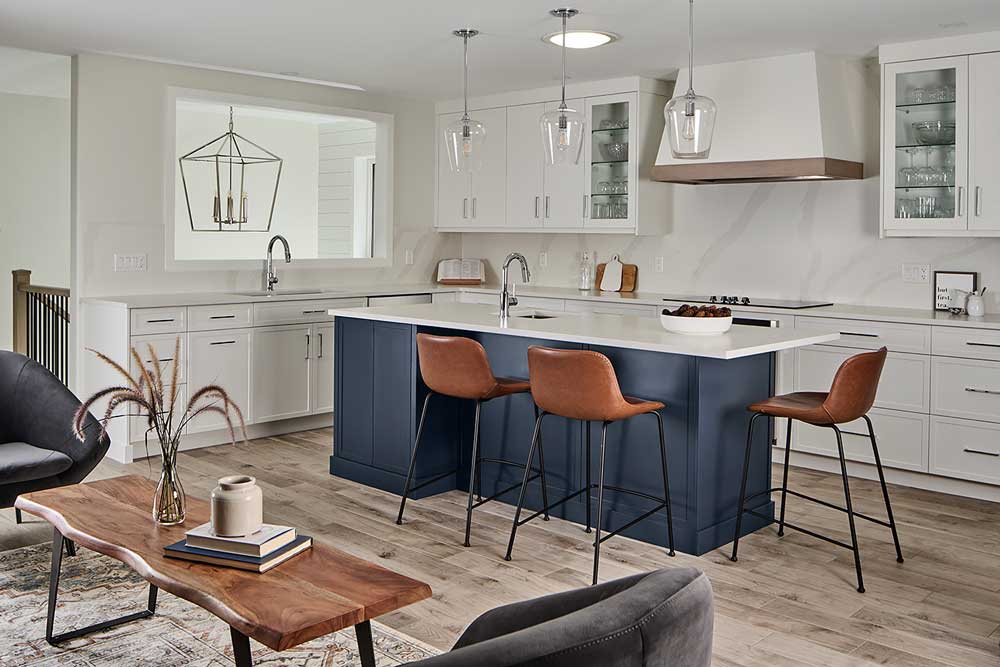 White kitchen cabinets against the wall, brown bar stools against the dark blue island base, and the wall cut out into the staircase area