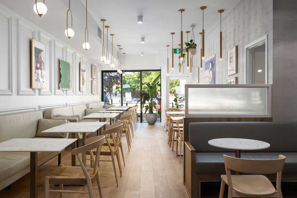 A view of the dining area looking toward the front of the restaurant with views of the streets. Stunning elegant pendants hang above and beautiful colourful artwork decorates the walls